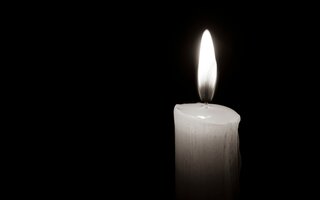 Brennende Kerze vor schwarzem Hintergrund in schwarz-weiß.